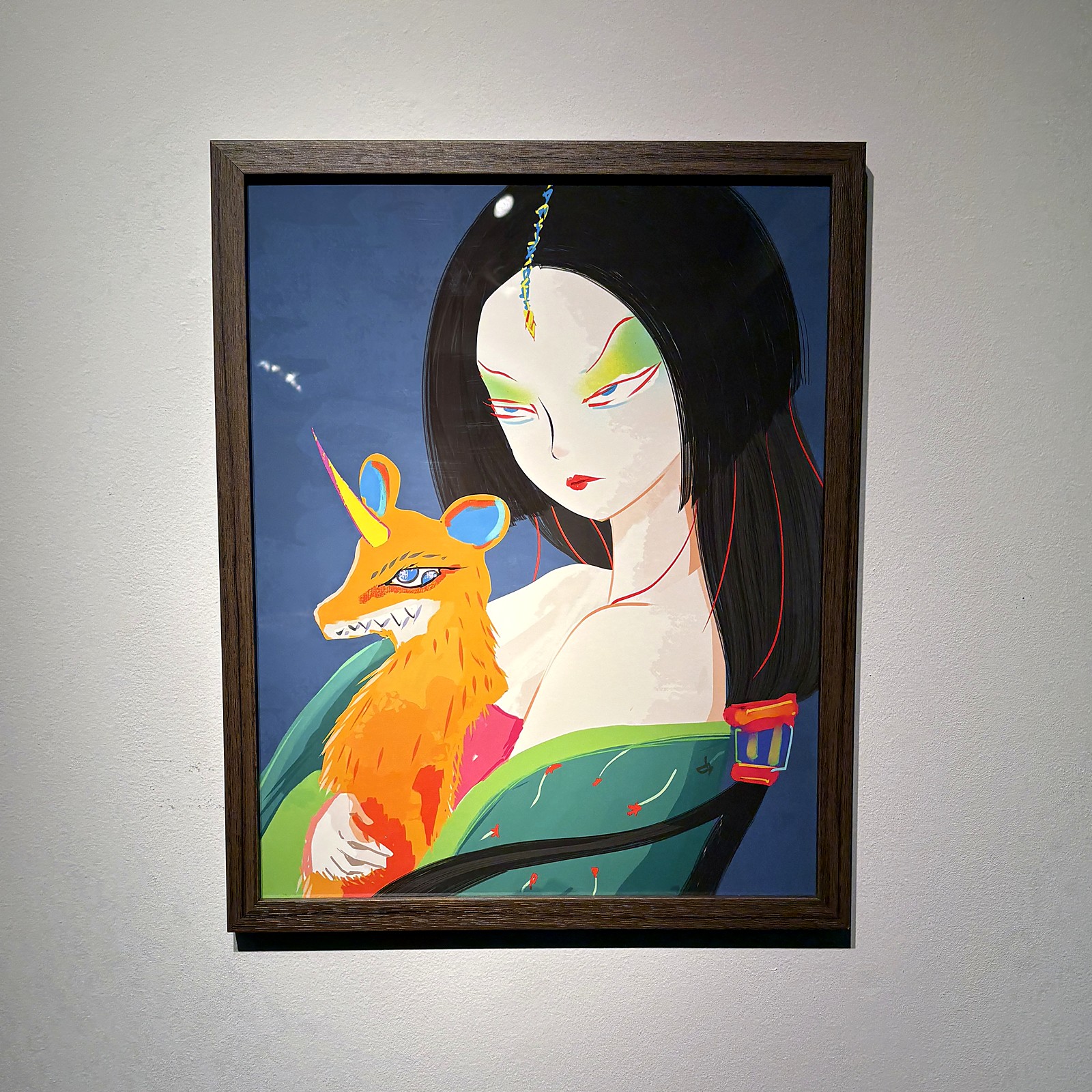 A dark wood frame on a white gallery wall: a woman holding an orange creature.