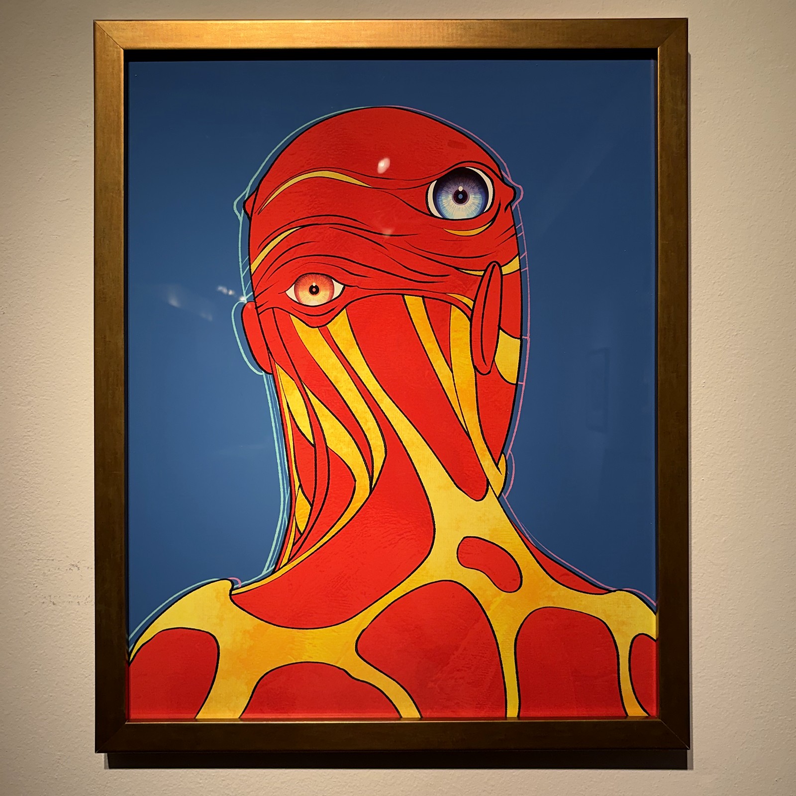 A gold frame on a white gallery wall: a red and gold figure on blue.