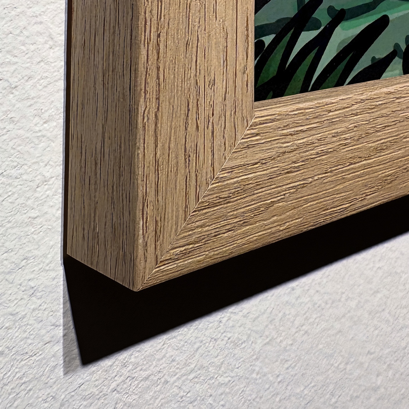 The corner of the pale oak frame, the grain left bare.